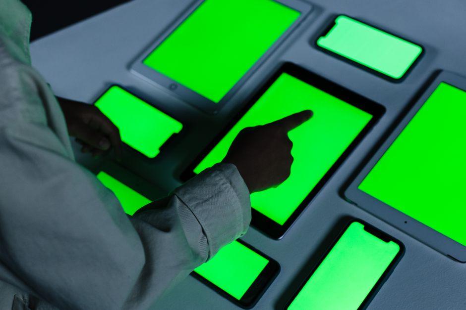 Person interacting with multiple green-screen electronic devices indoors